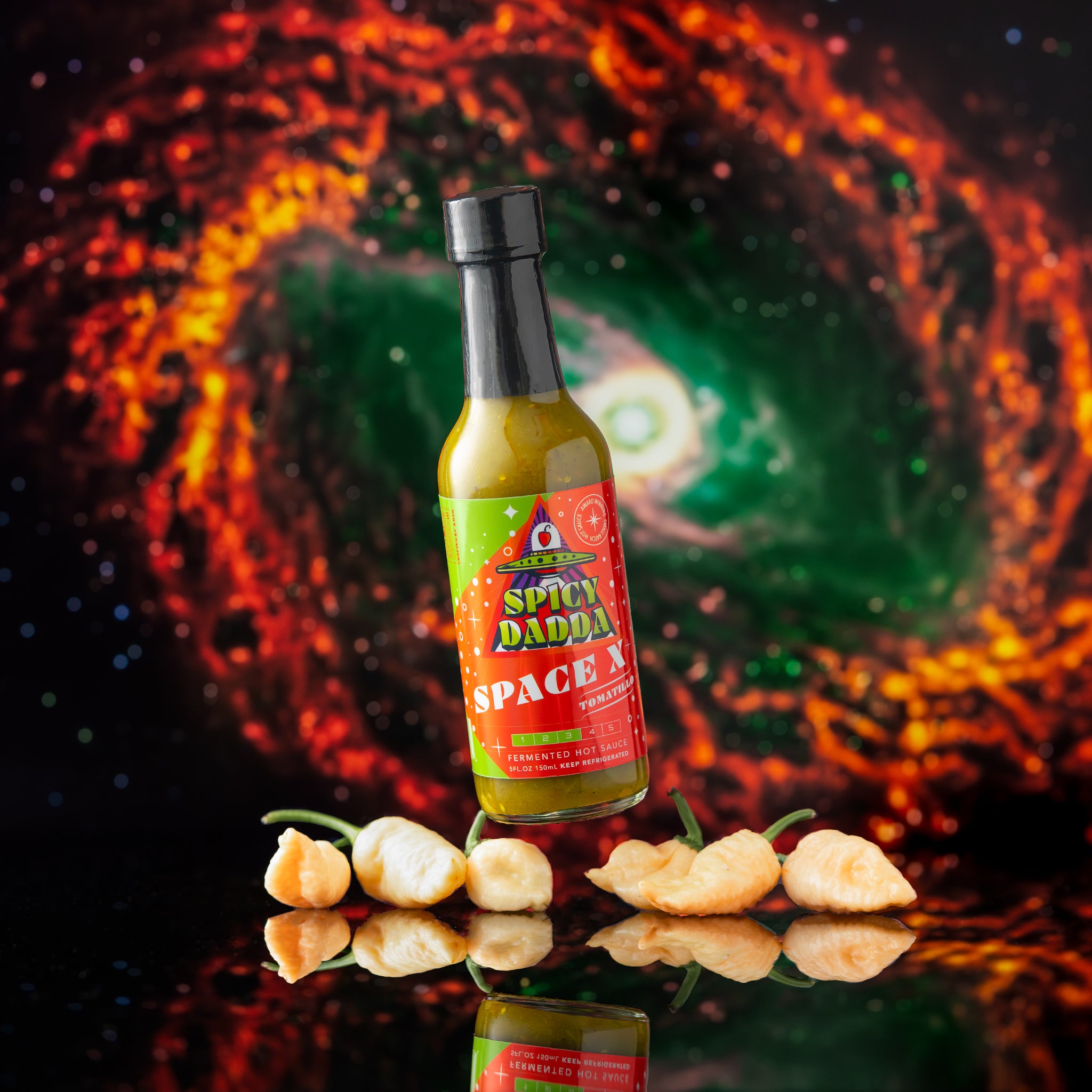 Spicy Dadda Space X Tomatillo fermented hot sauce bottle surrounded by fresh tomatillos and homegrown peach colored superhot peppers against a surreal cosmic background.