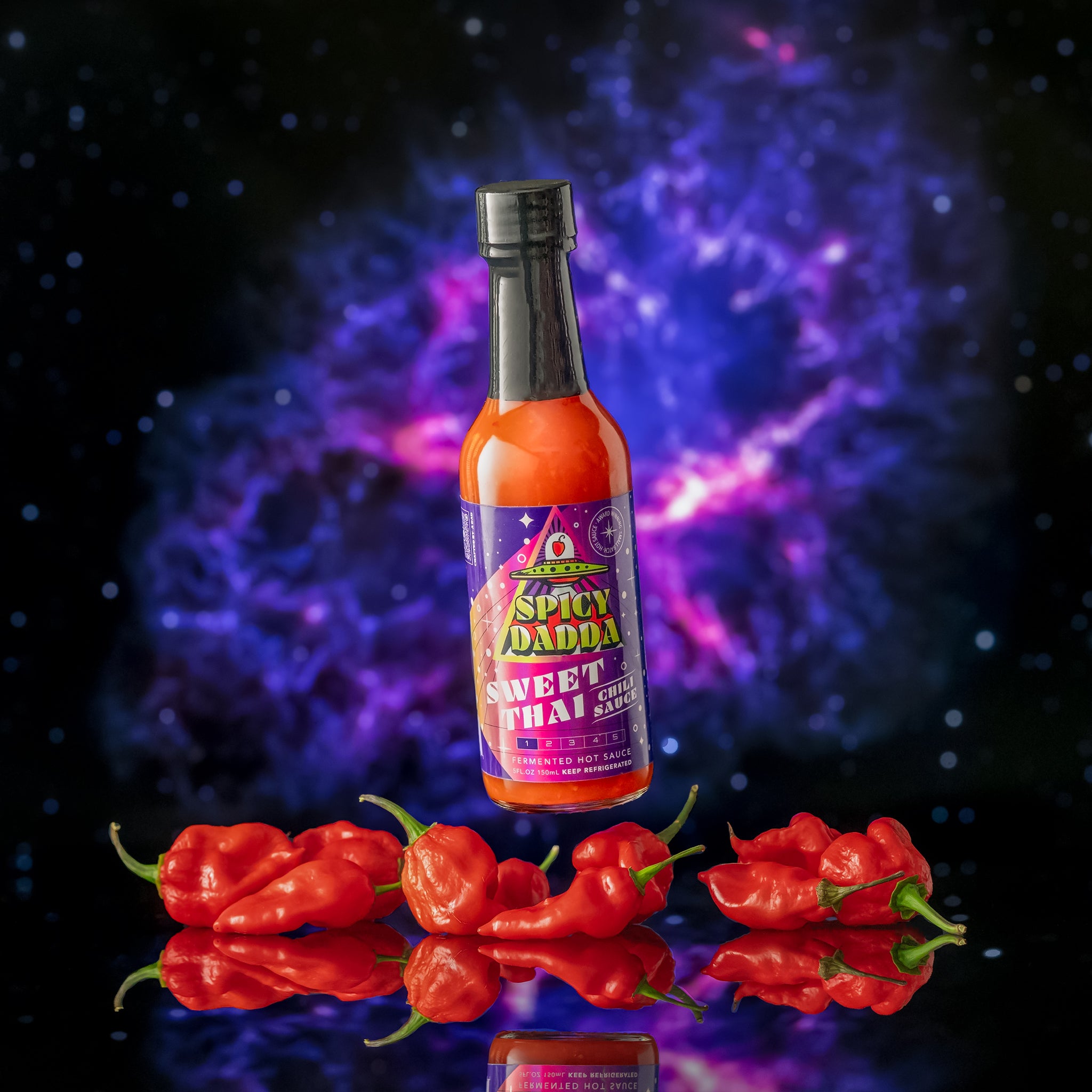 Spicy Dadda Sweet Thai Chilli fermented hot sauce bottle surrounded by fresh red chilli peppers against a glowing cosmic space background.